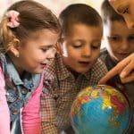 Group of children at preschool examining world globe with their teacher