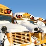 A row of school buses covered in snow