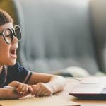 Little girl in glasses smiling looking at laptop