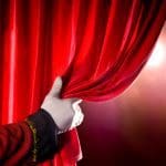 Usher opening red theater curtain, with spotlights