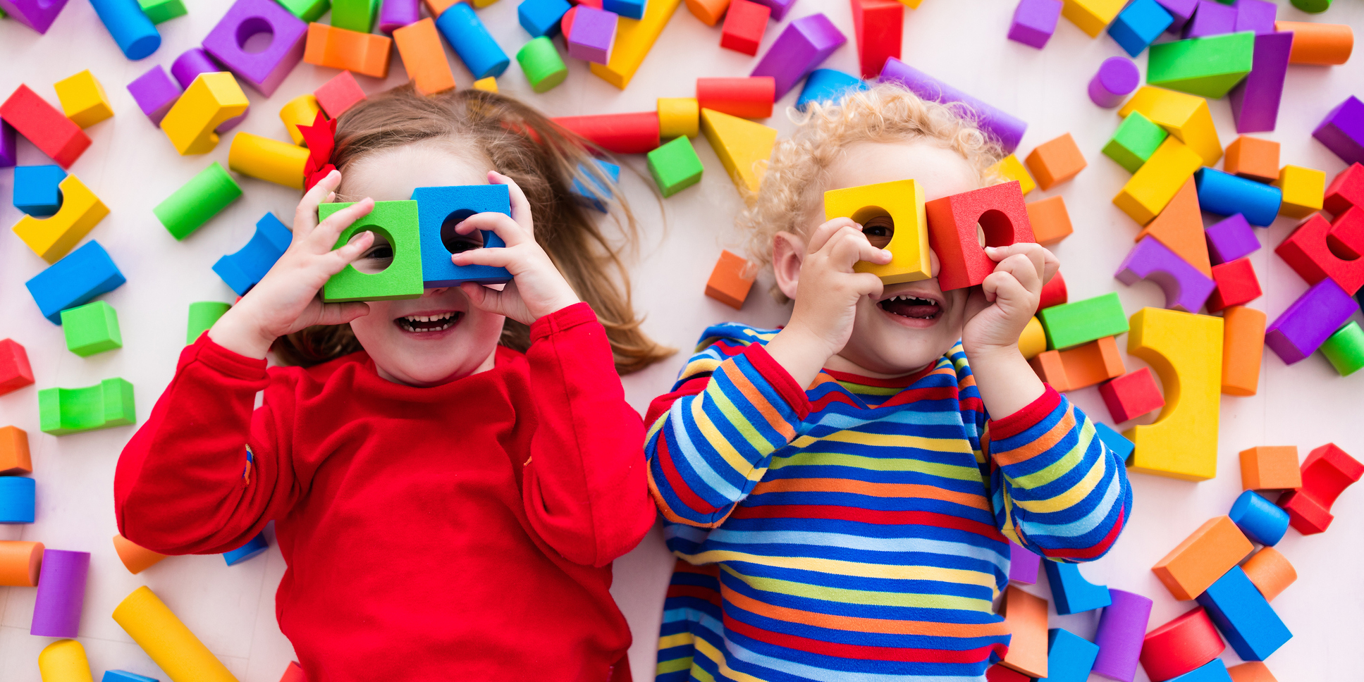 Happy preschool age children play with colorful plastic toy blocks