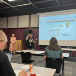 Teacher at front of classroom in front of a digital board