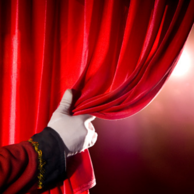 White gloved hand opening a red theater curtain