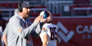 Man wearing a ball cap on a football field talking to players